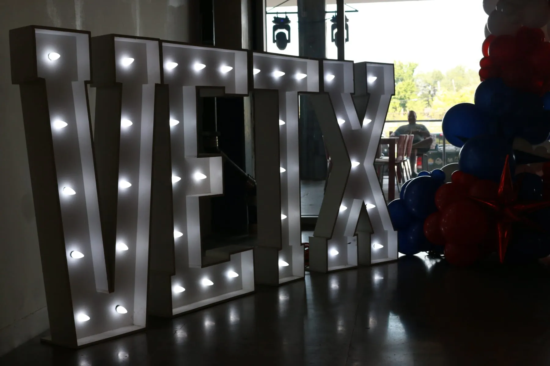 Large lighted event signage with red and blue balloons at a venue