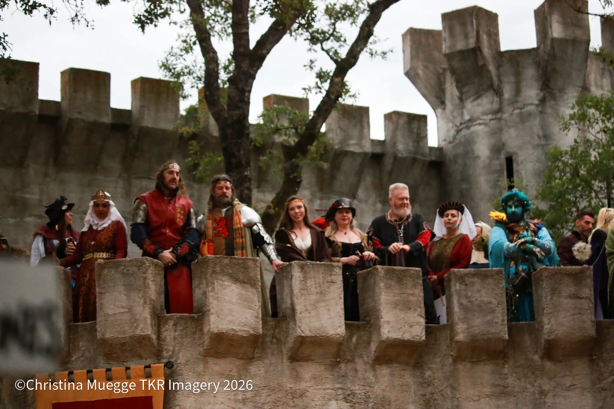 Costumed Renaissance festival performers gathered along a castle wall