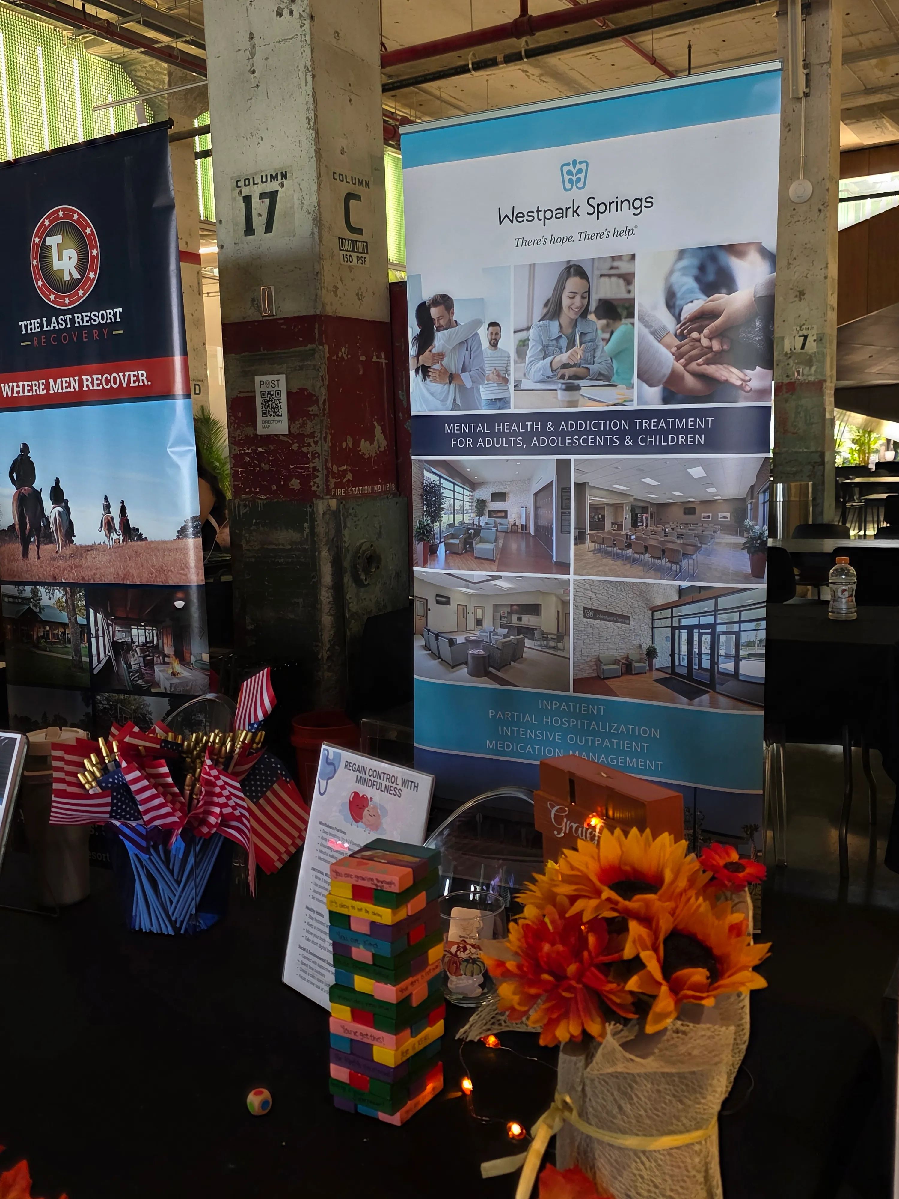 Sponsor and recovery organization display table with event materials, flags, and branded banners